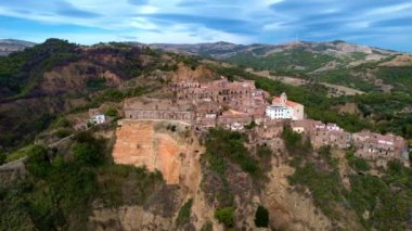 4K hava aracı videosu, gizemli bir görüntüyle tepelerde gerçek dışı bulut şekilleriyle yükseliyor. İtalya 'nın terk edilmiş Tursi kasabası. Boş evleri ve sokakları var.