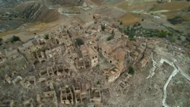 Tepenin tepesinde harabeler ve boş evler olan gizemli hayalet kasabanın 4K hava aracı videosu. Yıkılan yapıları ve yıkılan kilisesi olan lanetli bir köy. Terk edilmiş şehir Craco, Matera, İtalya