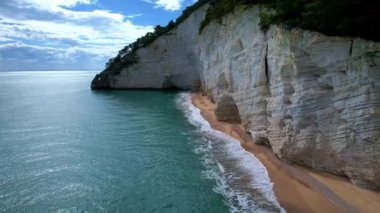 Güneşli bir günde, beyaz yüksek uçurumlar ve turkuaz mavi sularla çevrili en büyüleyici kumlu kumsalın 4K hava aracı videosu. İtalya, Apulia 'daki büyüleyici Vignanotica plajı