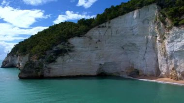 Güneşli bir günde, beyaz yüksek uçurumlar ve turkuaz mavi sularla çevrili en büyüleyici kumlu kumsalın 4K hava aracı videosu. İtalya, Apulia 'daki büyüleyici Vignanotica plajı