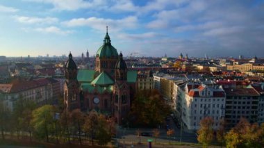 Münih şehir merkezinde güneşli bir günde Isar Nehri, Saint Lukas Kilisesi, Marienplatz ve Maximilianeum ile güzel bir sonbaharın 4K hava aracı videosu, Almanya