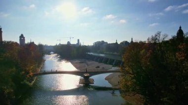 Münih şehir merkezinde güneşli bir günde Isar Nehri, Saint Lukas Kilisesi, Marienplatz ve Maximilianeum ile güzel bir sonbaharın 4K hava aracı videosu, Almanya