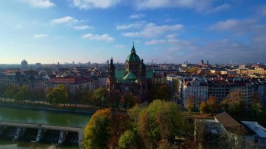Münih şehir merkezinde güneşli bir günde Isar Nehri, Saint Lukas Kilisesi, Marienplatz ve Maximilianeum ile güzel bir sonbaharın 4K hava aracı videosu, Almanya