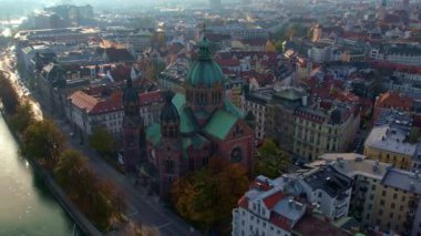 Münih şehir merkezinde güneşli bir günde Isar Nehri, Saint Lukas Kilisesi, Marienplatz ve Maximilianeum ile güzel bir sonbaharın 4K hava aracı videosu, Almanya