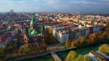 Münih şehir merkezinde güneşli bir günde Isar Nehri, Saint Lukas Kilisesi, Marienplatz ve Maximilianeum ile güzel bir sonbaharın 4K hava aracı videosu, Almanya