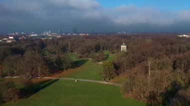 Monopteros ve Çin kulesinin 4K hava aracı videosu, Münih Almanya 'nın tarihi simgeleri güneşli ve sisli bir sonbahar gününde şehir panoramasına bakan İngiliz Bahçesi kamu parkı