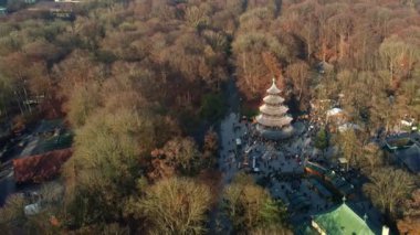 Monopteros ve Çin kulesinin 4K hava aracı videosu, Münih Almanya 'nın tarihi simgeleri güneşli ve sisli bir sonbahar gününde şehir panoramasına bakan İngiliz Bahçesi kamu parkı