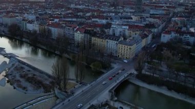 Münih Almanya 'nın Münih kentinde güneşli bir günde gün batımında şehir panoramasına bakan Isar nehrinin merkezindeki St. Maximilian Kilisesi' nin 4K hava aracı videosu.