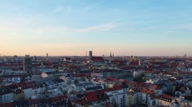 Münih Almanya 'nın Münih kentinde güneşli bir günde gün batımında şehir panoramasına bakan Isar nehrinin merkezindeki St. Maximilian Kilisesi' nin 4K hava aracı videosu.