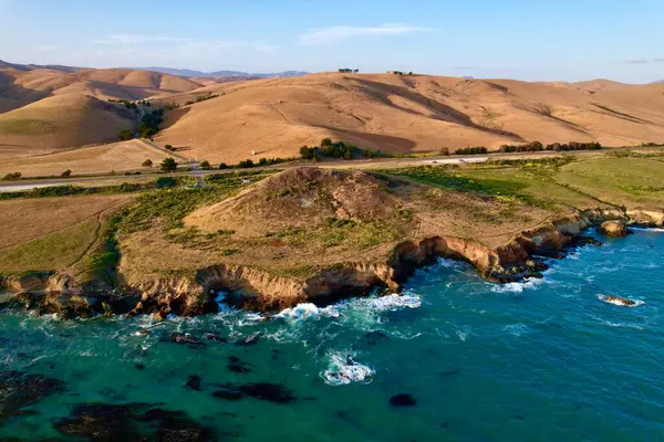 Dünyaca ünlü Karayolu 1 Batı Kıyısı California 'nın havadan görünüşü. Estero Bluffs Eyalet Parkı. Gün batımında dalgalar güzel kayalıklara çarpıyor. Altından bir saat sonra otoyol tam yanında akıyor.