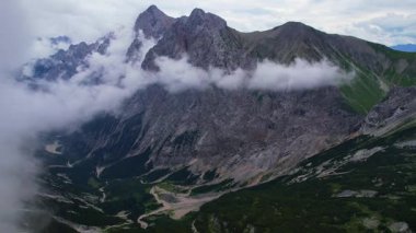 Almanya 'nın en yüksek dağ zirvesine yapılan yürüyüşün 4K Hava Aracı videosu, destansı bulutlar ve inanılmaz doğa ile kasvetli sisli bir günde Zugspitze. Ünlü dağ kulübesi Knorr Hut