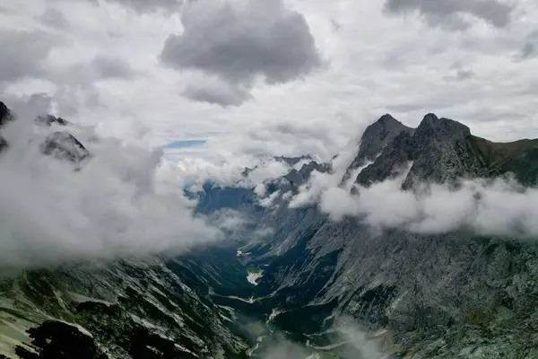 Almanya 'nın en yüksek dağ zirvesine yapılan yürüyüşün 4K Hava Aracı videosu, destansı bulutlar ve inanılmaz doğa ile kasvetli sisli bir günde Zugspitze. Ünlü dağ kulübesi Knorr Hut