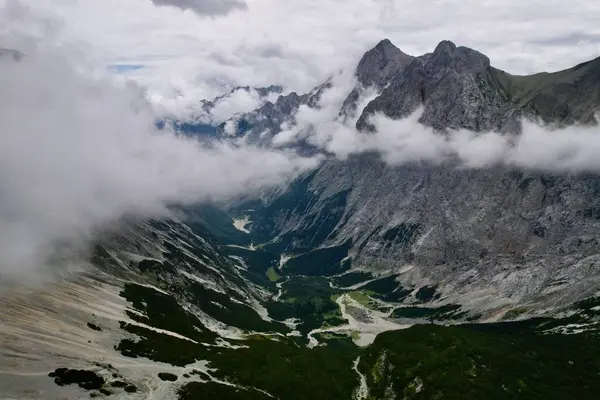 Almanya 'nın en yüksek dağ zirvesine yapılan yürüyüşün 4K Hava Aracı videosu, destansı bulutlar ve inanılmaz doğa ile kasvetli sisli bir günde Zugspitze. Ünlü dağ kulübesi Knorr Hut