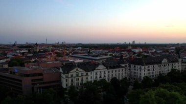 Münih şehir merkezinde sabahın erken saatlerinde St Lukas Kilisesi, Isar Nehri, Marienplatz ve Barış Meleği Friedensengel 'e bakan sessiz bir hava aracı videosu. Mor bir gündoğumunda güzel bir gökyüzü