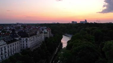 Münih şehir merkezinde sabahın erken saatlerinde St Lukas Kilisesi, Isar Nehri, Marienplatz ve Barış Meleği Friedensengel 'e bakan sessiz bir hava aracı videosu. Mor bir gündoğumunda güzel bir gökyüzü