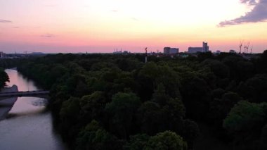 Münih şehir merkezinde sabahın erken saatlerinde St Lukas Kilisesi, Isar Nehri, Marienplatz ve Barış Meleği Friedensengel 'e bakan sessiz bir hava aracı videosu. Mor bir gündoğumunda güzel bir gökyüzü