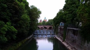 Münih şehir merkezinde sabahın erken saatlerinde St Lukas Kilisesi, Isar Nehri, Marienplatz ve Barış Meleği Friedensengel 'e bakan sessiz bir hava aracı videosu. Mor bir gündoğumunda güzel bir gökyüzü
