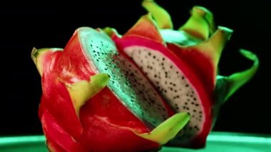 4k footage of rotating cutting into two pieces dragon fruit. Juicy and fresh fruit with pink skin and white flesh in the middle against a dark background. Pitaya is a healthy food with a lot vitamins.