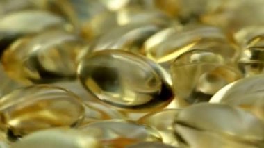 4k yakın çekim, şeffaf jöle tabletleri saat yönünde dönüyor. İçinde yağlı sarı sıvı olan haplar. Sağlıklı vitaminler ışıkta parıldıyor. D vitamini, Omega 3, yağ asitleri.