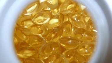 4k yakın çekim üst görüntü şeffaf jöle tabletleri saat yönünde döner. İçinde yağlı sarı sıvı olan haplar. Sağlıklı vitaminler ışıkta parıldıyor. D vitamini, Omega 3, yağ asitleri.