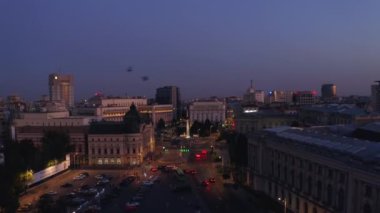 4K Drone görüntüleri. Romanya 'nın başkenti Bachares' te akşam yemeği. Bir sürü kuş gün batımından sonra yanan şehir ışıklarının arka planına karşı ön planda uçar. Sokaklarda trafik vardı.