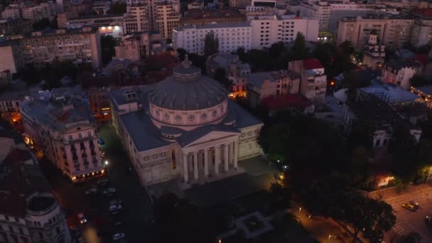 ドローン映像 カメラはブカレストの中心にあるコンサートホールであるルーマニアのアテナイの景色を明らかにします ルーマニアの首都の主要なランドマークの一つ 夕暮れの街ライト — ストック動画