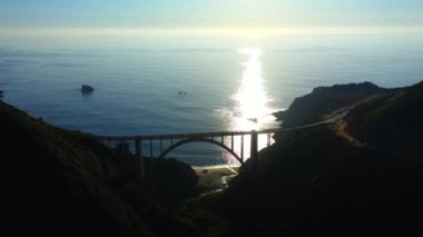 4k sinematik hava manzaralı gün batımı. Mavi Pasifik Okyanusu 'nun arka planına karşı Bixby Creek Köprüsü üzerinde panoramik hava manzarası. Güneş ufukta dalgalara batıyor. Big Sur 'un Doğası. 