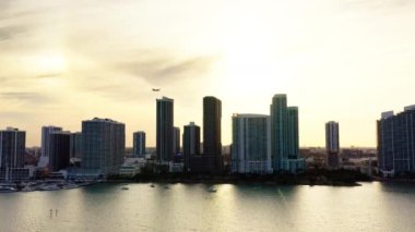 Günbatımında Miami City 'nin 4k sinematik görüntüsü. Biscayne Körfezi kıyısının ilk hattındaki yatların ve yüksek binaların sularından görüntü. Uçak altın gökyüzünde uçuyor. Florida ABD