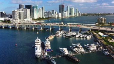 Biscayne Körfezi 'ndeki yatların 4k manzarası. Yat işi için güzel bir ağır çekim drone videosu. Arka planda modern metropolün yüksek binaları ve yoğun trafiği olan köprüler var. Miami