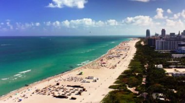 4k drone fooatge. El değmemiş beyaz kumu ve turkuaz sularıyla Miami Sahili 'nin göz kamaştırıcı manzarası. Kıyı şeridi plaja gidenlerle dolu ve yüksek binalar ve otellerle dolu..