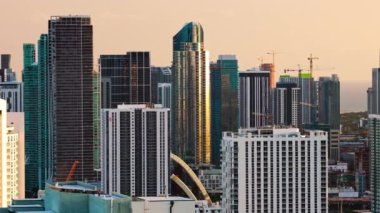 4K Miami şehir merkezindeki şehir silueti gün batımında. Modern gökdelenlerin ve hareketli inşaatın yer aldığı, batan güneşin aydınlattığı şehrin sofistike ve canlı yaşamını yansıtıyor..