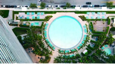 Yeşil palmiye ağaçları, güneş pansiyonları ve yüksek binalarla çevrili lüks Miami havuzu manzarası. Mükemmel güneşli bir gün manzarası. Şehir eğlencesi ve rahatlama. 4k görüntü