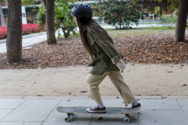 Genç kaykaycı kadın parkta sörf tahtası ile numara yapıyor. Hobi ve spor konsepti.