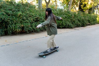 Genç kaykaycı kadın parkta sörf tahtası ile numara yapıyor. Hobi ve spor konsepti.