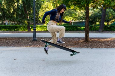 Genç kaykaycı kadın parkta sörf tahtası ile numara yapıyor. Hobi ve spor konsepti.