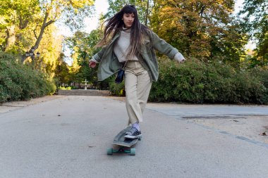 Genç kaykaycı kadın parkta sörf tahtası ile numara yapıyor. Hobi ve spor konsepti.