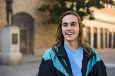 Man smiling while sitting on bench outdoors on the street.