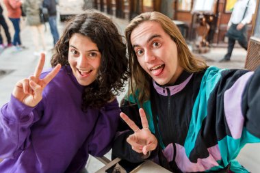 Two friends taking a selfie while sitting on a table outdoors. Friendship concept.