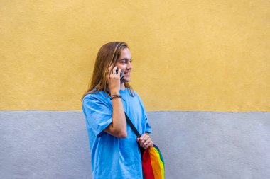Man talking on the phone while wearing a belt bag with the lgbt rainbow flag. Technology and lgbt concept.