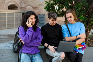 Dışarıda dikilirken dizüstü bilgisayar ve cep telefonu kullanan Igbt gökkuşağı bayraklı genç insanlar. Lgbt ve teknoloji kavramı.