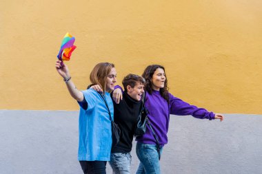 Young diverse friends embracing each other while walking on the street with pride rainbow flag. Lgbtq concept.