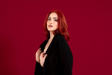 Kızıl saçlı, kendine güvenen, kameraya bakan ve kırmızı izole bir arkaplanda poz veren bir kadının yakın çekimi..