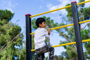 Genç bir çocuk parkta çocuk parkına tırmanırken eğleniyor. Çocukluk kavramı.