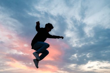 Arka planda gün batımı gökyüzü ile atlayan bir kişinin silueti.