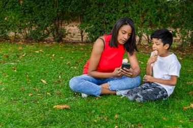 Anne ve oğlu dondurma yemekten ve cep telefonuna bakmaktan zevk alıyorlar. Aile, yemek ve yaz konsepti.