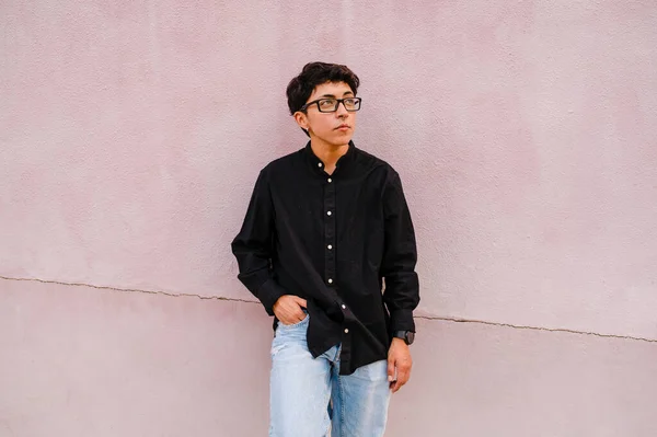 stock image Young transgender man with glasses leaning on a wall while posing outdoors on the street.