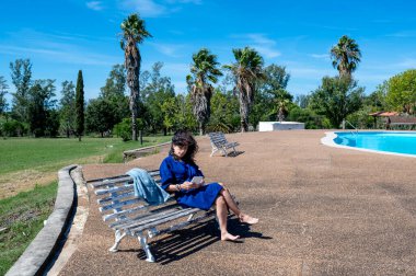 Güneşli bir günde dışarıda otururken kitap okuyan bir kadın. Teknoloji ve tatil kavramı.