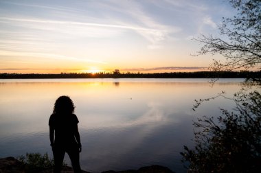 Gün batımında göl kenarında yürüyen gezgin kadın. Doğa ve seyahat kavramı.