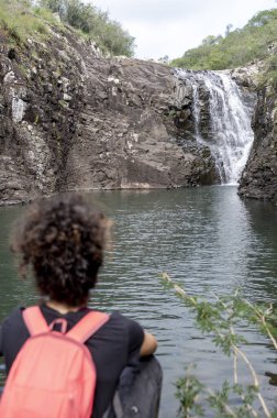 Sırt çantalı gezgin kadın doğada dinlenirken şelaleye bakıyor. Seyahat, macera ve doğa konsepti.