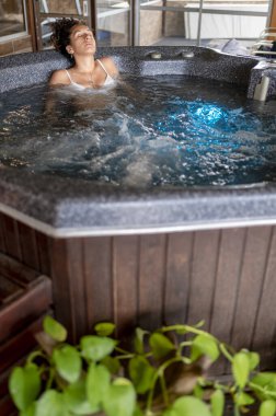 Gözleri kapalı bir kadın jakuzide dinlenirken spa gününün tadını çıkarıyor..